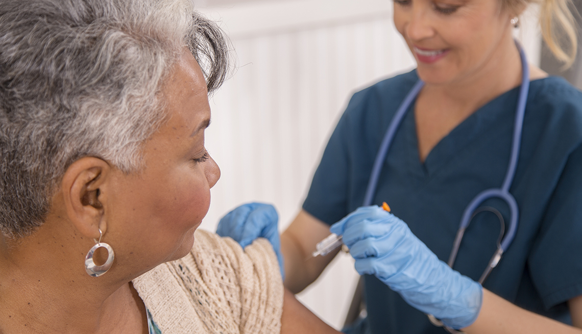 Nurse gives flu vaccine to African descent, senior adult patient at a local pharmacy, clinic, or doctor's office.