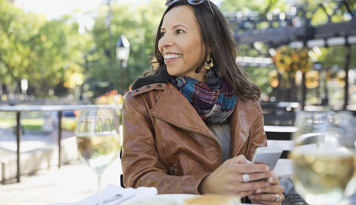 Woman in leather jacket sitting at outdoor cafe with smartphone